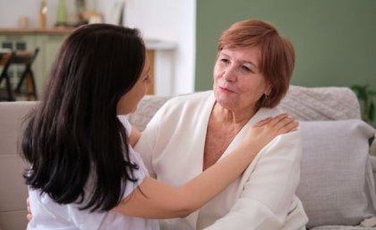 Cognitive changes make it difficult for older people to challenge internalised ageist beliefs. Image: Adobe A woman with long dark hair and a woman with short red hair embrace while sitting on a white sofa.